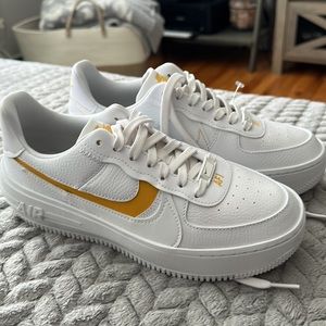 Nike Air Force one sneakers with mustard yellow accents.